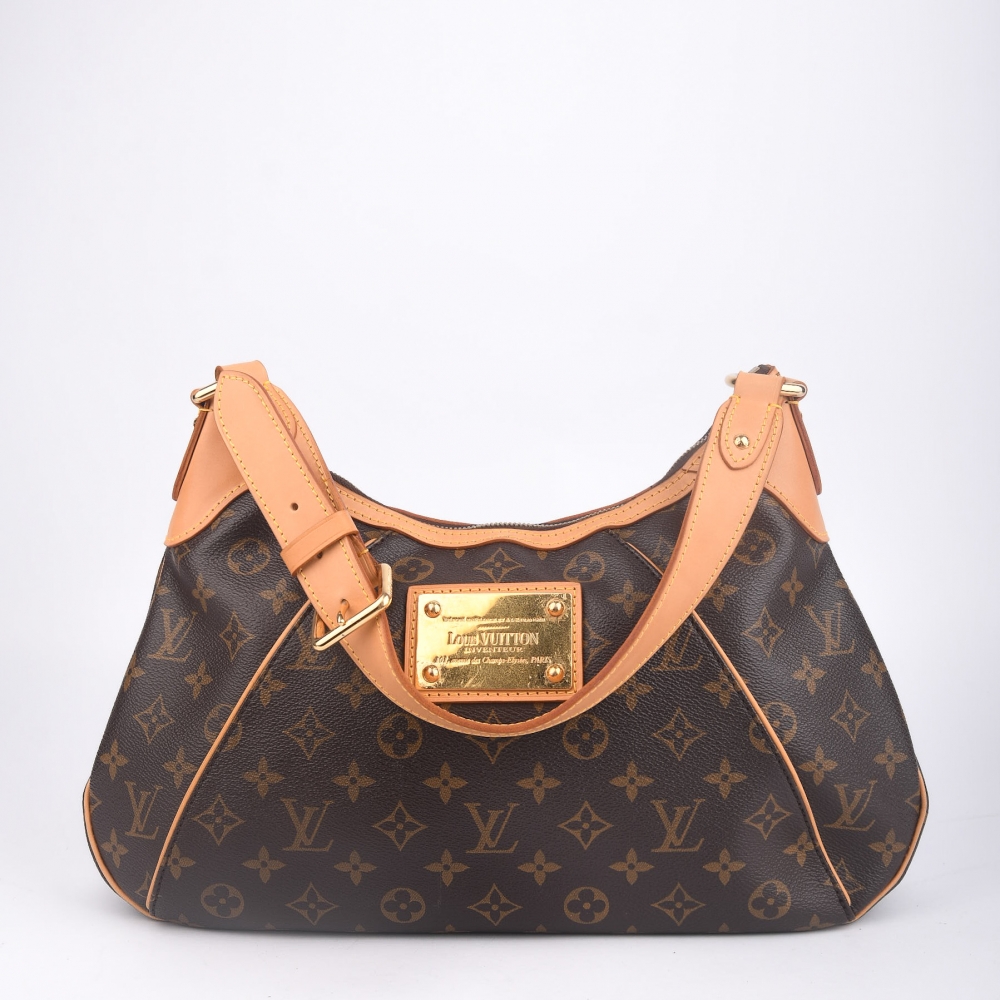 En moderne og elegant Louis Vuitton Thames fra 2010, laget i brun monogram canvas med gullfarget hardware og helt nytt skinn. Produsert i Frankrike, og kjent for sin buede silhuett, metallplakett i front og komfortable bærelengde 