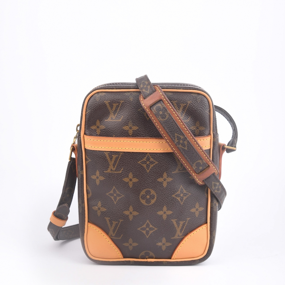 En klassisk og kompakt crossbody-veske fra Louis Vuitton – modellen Danube, laget i ikonisk brun monogram canvas med gullfarget hardware og helt nytt skinn. Produsert i Frankrike i 2004, og kjent for sin praktiske størrelse og tidløse stil. 