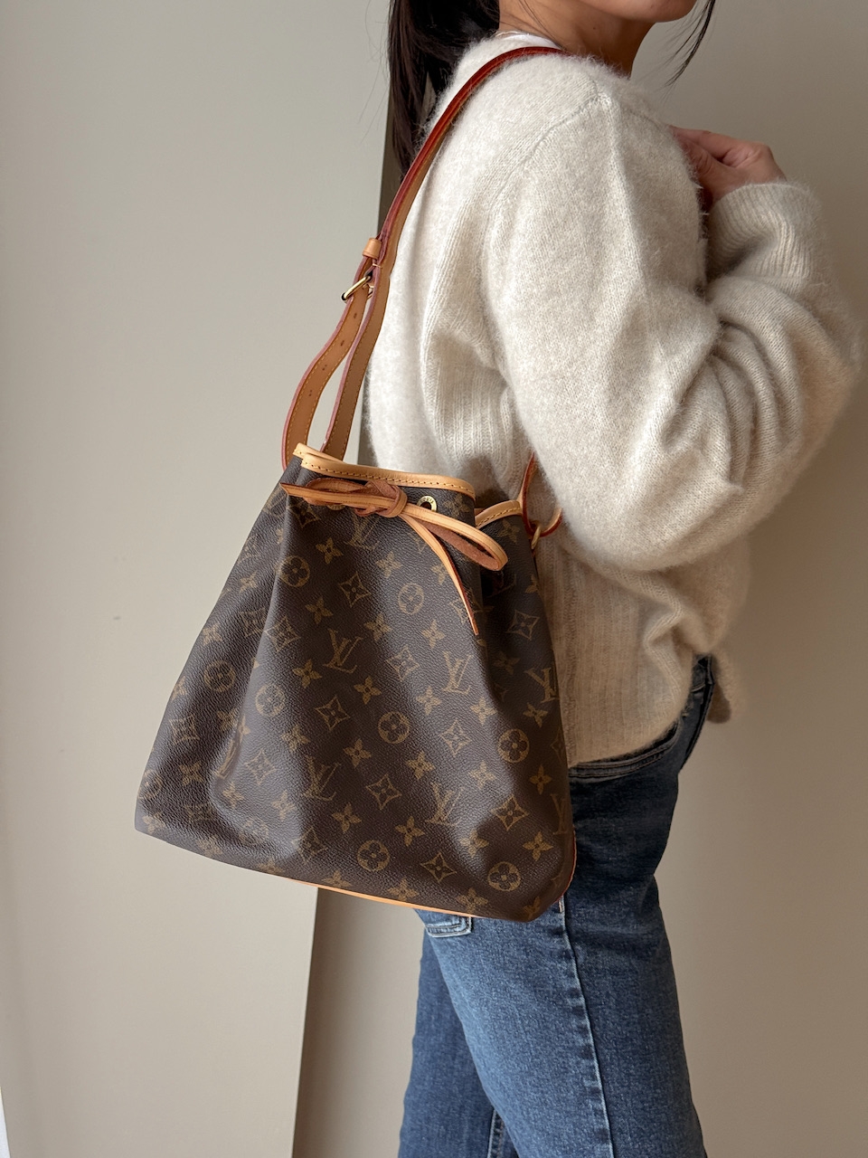 En tidløs og funksjonell bøtteveske fra Louis Vuitton – modellen Noé PM, laget i slitesterk brun monogram canvas med ekte skinn og gullfarget hardware. Vesken ble opprinnelig designet for å bære champagneflasker, men fungerer i dag som en stilig og romsli