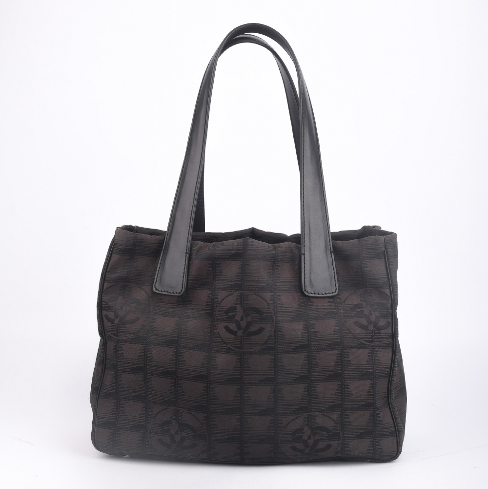 En ikonisk og lett Chanel Travel Line Tote  laget i sort nylon med det klassiske CC-rutemønsteret og sølvfarget hardware. Produsert i Frankrike i 2004, og kjent for sin funksjonelle eleganse og holdbare konstruksjon – et perfekt valg for både hverdagsbruk